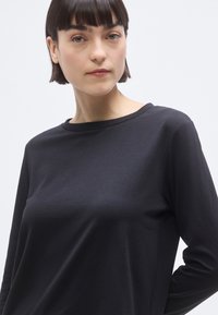 Haut noir à manches longues avec un col rond. Texture douce, coupe ajustée et style minimaliste. Aucun motif ou détail métallique visible.
