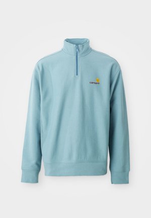 Pull-over bleu clair à manches longues avec col zippé moitié et petit logo Carhartt orange et marron sur la poitrine gauche.