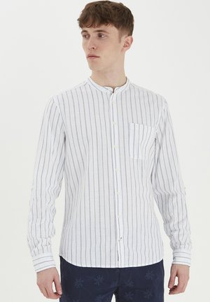 Hvit langermet skjorte med blå vertikale striper, ståkrage og lomme på venstre bryst. Stoffet ser lett og teksturert ut.