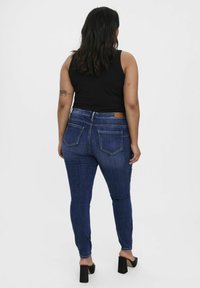 Kitsase sinine denim teksad sisaldavad kõrget taljeosa, kahte tagaTaskut ja pruunist nahast brändi silt. Ühendatud musta tank topi ja kontsadega.
