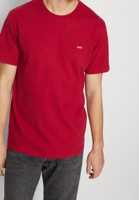 Červené bavlněné tričko s kulatým výstřihem a krátkými rukávy. Na levé hrudi je malé bílé logo Levi's. Nosit s šedými džíny.