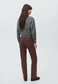 Sivi rebrasti pulover uparen s smeškim širokim trapericama s bočnim dugmadima. Mekane teksture kontrastiraju s glatkom, umjerenom pozadinom.