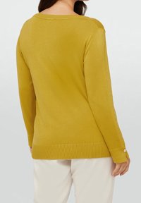 Pullover color senape con vestibilità morbida e orlo a costine. Presenta dettagli con bottoni sulle maniche e un ampio scollo, realizzato in tessuto morbido.
