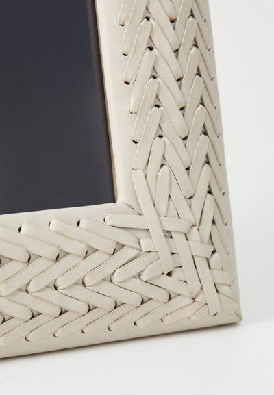 Quadro incorniciato con un bordo in faux leather intrecciato e testurizzato di colore crema chiaro, che presenta uno sfondo nero liscio.