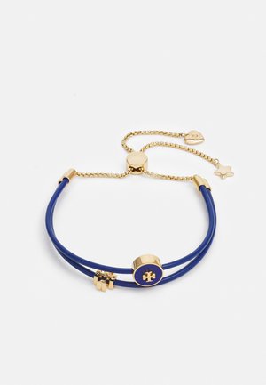 Pulsera ajustable con doble cordón azul, pieza central con charm en forma de pieza de puzzle en tono dorado y cadena dorada con charms de corazón y estrella.