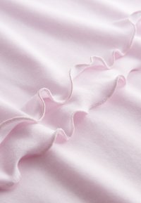 Rosa Stoff mit glatter Textur besitzt einen welligen, gerafften Rand mit satinartiger Oberfläche. Die Rüsche hat eine zarte, glänzende Umrandung.