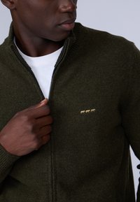 Cardigan zippé vert olive en tricot doux, doté d'un col montant et d'un motif animal en tricot jaune subtil sur la poitrine.