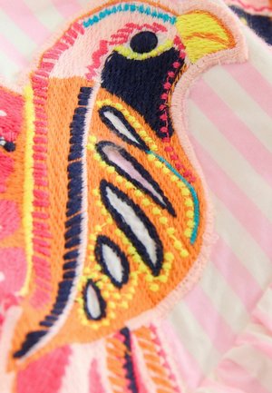 Nahaufnahme eines farbenfrohen, bestickten Vogels mit orangefarbener, gelber, schwarzer, rosa und blauer Stickerei auf einem hellrosa gestreiften Stoffhintergrund.
