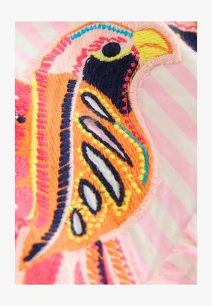 Detailný záber farebne vyšívaného vtáka s čiarou v farbách oranžová, žltá, čierna, ružová a modrá na svetloružovom pruhovanom látkovom pozadí.