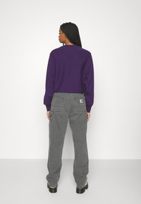 Purple sweatshirt with a crew neck, paired with light gray cargo pants featuring patch pockets and a label on the back. Black chunky footwear visible.