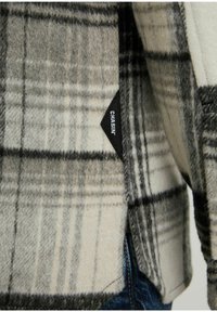 Ruudullinen villakangastakki vaaleassa, harmaassa ja mustassa värissä. Siinä on "CHASIN'"-tunnus sivussa, pehmeä rakenne ja istuva leikkaus.