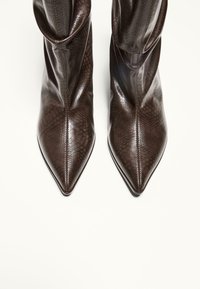 Boots de glezna din piele maro, cu o textură de piele de șarpe, design cu vârf ascuțit și cusături verticale, având un șliț înalt și un finisaj neted.