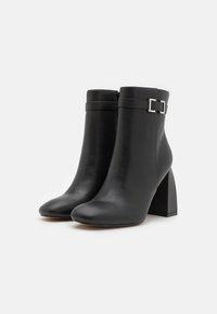 Botines de cuero negro hasta el tobillo con puntera redonda y tacón grueso. Presentan una correa decorativa y un detalle de hebilla cerca de la parte superior.