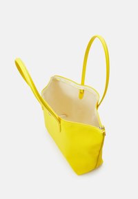 Sac cabas jaune en matériau lisse et structuré, avec des anses fines et un intérieur spacieux doté d'une doublure claire et d'une marque discrète.