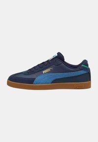 Zapatilla de ante en azul marino y azul claro con suela de goma, que presenta un logotipo dorado y una lengüeta acolchada. Cordones y detalles cosidos visibles.