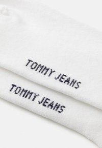 Two white cotton socks with black "TOMMY JEANS" text embroidered near the cuff on a white background.