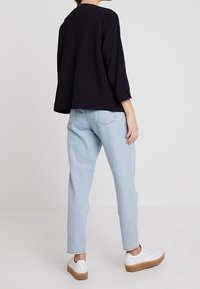 Marinblus i struktur med trekvartslånga ärmar, parat med ljusblå jeans och vita sneakers med en beige gummisula.