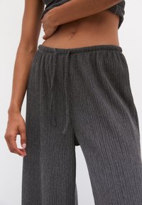 Grå ribbade vida byxor med elastisk midja och dragsko. Mjuk textur med vertikala ränder, med en lös passform.