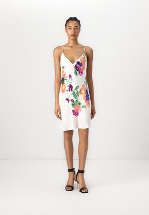 White short dress with a V-neck, featuring colorful floral embroidery in orange, pink, purple, and green. Worn with black strappy heels.
