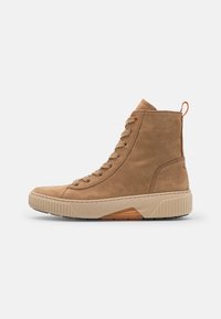 Tan high-top boots made of suede with a textured rubber sole, featuring round laces and a contrasting orange pull tab.