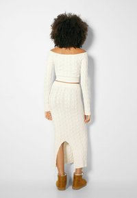 White cable knit cropped sweater with long sleeves, paired with a matching midaxi skirt featuring a back slit, worn with tan boots.