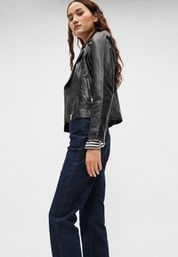 Mustast nahast mootorratturi jakk hõbedaste tõmblukkudega, istuva lõikega ja triibuliste varrukaservadega. Kandmiseks kombineeritud tume siniste kõrge vöökohaga teksadega.