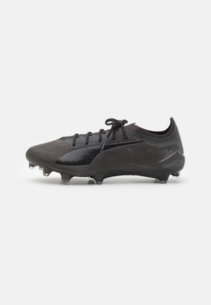 Crampons de football noirs avec une tige texturée, présentant un design épuré, un système de laçage et des crampons métalliques pour une traction sur le terrain.
