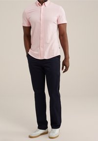 Světle růžová košile s krátkým rukávem a kravato-cíleným límcem, kombinovaná s tmavě námořnickými chinos kalhotami a bílými teniskami s gumovou podrážkou. Celkově hladká textura.