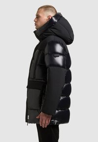 Musträbal must jacket, mille läikiv viimistlus, ülekasvanud kapuuts, lukuga ja floki taskud ning paneelide disain. Varrukal on logo.
