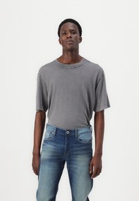 Grå överdimensionerad t-shirt med kort ärm och rund hals, parat med blå denimjeans med gradient som har knäppning och framfickor.