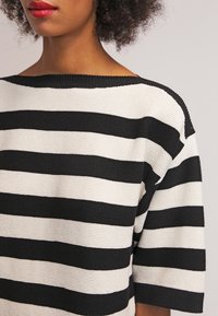 Czarnobiały sweter w paski z szerokim dekoltem, krótkimi rękawami i teksturowanym wzorem dzianiny, z wyraźnymi poziomymi paskami.