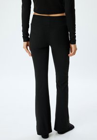 Pantalones de campana negros en un material suave y elástico con una cintura alta. La textura es lisa, sin patrones visibles ni detalles de hardware.