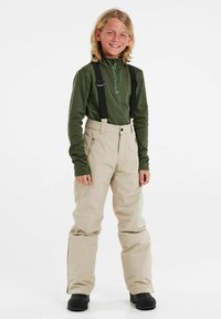 Beige Schnee-Hosen mit verstellbaren schwarzen Trägern, kombiniert mit einem dunkelgrünen langärmeligen Baselayer. Die Hose hat Reißverschlusstaschen.