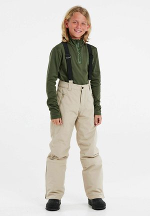 Beige sneaks med justerbare sorte bælter, parret med en mørkegrøn langærmet baselayer. Bukserne har lynlåslommer.