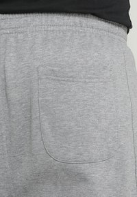 Pantalones de chándal grises con cintura elástica, textura suave, con un único bolsillo trasero de bordes limpios y sin logotipos ni adornos visibles.