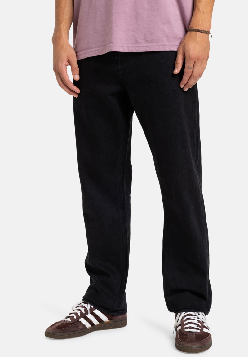 Pantalones de mezclilla negros con corte recto. Combinados con zapatillas deportivas marrones y blancas. Textura suave, detalles mínimos y sin marcas visibles.