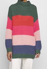 Neulepullover korkealla kauluksella, jossa on vaakasuoria raitoja vihreänä, punaisena, vaaleanpunaisena ja laivastonsinisenä. Kankaan rakenne ja ribbireunat.