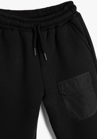 Pantalones de chándal negros con cinturilla elástica, cordón y una tela texturizada. Presenta un bolsillo lateral con un acento de tela suave.