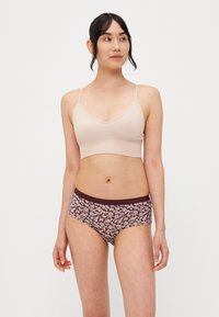 Top scurt din tricot bej cu bretele subțiri, asortat cu chiloți hipster purpurii cu flori, având un brâu solid. Textura materialului este netedă.