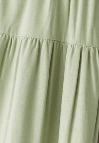 Svetlozelená látka s jemnou textúrou, so skladmi pozdĺž švov, ktorá vytvára objem a hladký záves.