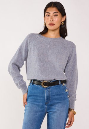 Maglione grigio lavorato a maglia con una vestibilità comoda, collo rotondo e maniche raglan, abbinato a jeans blu a vita alta e una cintura nera con fibbia dorata.