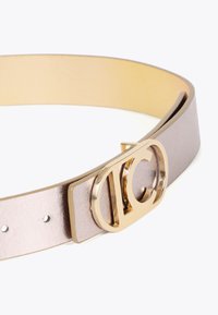 Tunn metallisk bälte i ljuslila läder med en slät yta, prytt med en cirkulär spänne i guldton med ett utskärningsmönster.