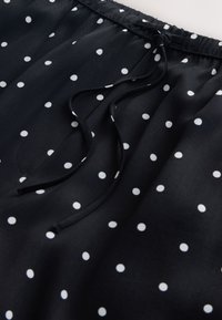 Fekete anyag fehér pöttyökkel, elasztikus derékpánttal és laza masnira kötött fekete zsinórokkal.