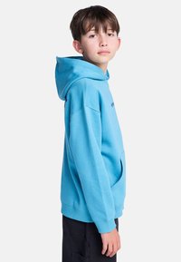 Felpa blu con cappuccio realizzata in tessuto morbido, con tasca frontale a marsupio e polsini a coste. Il modello la indossa mostrata di profilo.