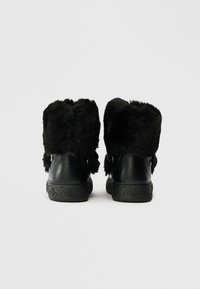 Black ankle boots featured with a faux fur collar, smooth leather body, textured black sole, and decorative hardware accents on the sides.