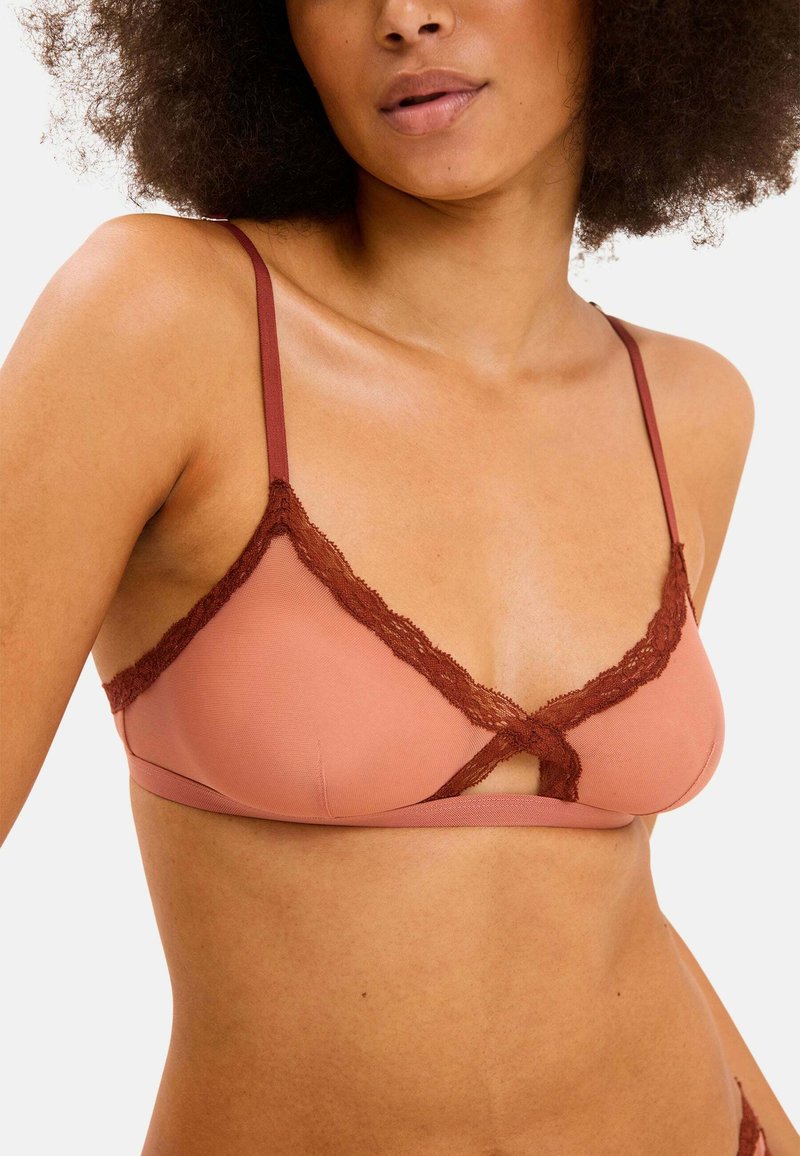 Ruskea pitsireunuksilla varustettu bralette, jossa on pehmeä vaaleanpunainen pohja, ohuet olkaimet ja kierretty etuosan muotoilu. Sujuva pinta ja minimaalinen peittävyys.