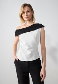 Off-shoulder topp med hvit kropp og svart krage. Strukturert stoff med side rynking. Brukt med svarte skreddersydde bukser.