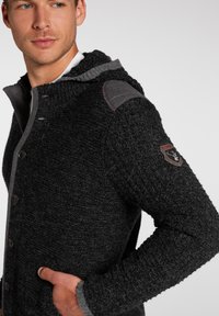 Knicke cardigan aus Kohlenstoff mit einer strukturierten Kapuze, Knopfverschluss, Taschen und grauen Schulterakzenten. Verfügt über einen strukturierten Stoff und ein Logo-Patch.