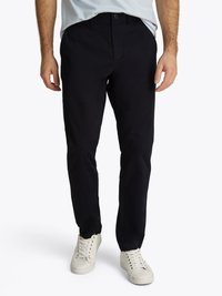 Chinos azul marinho feitos de algodão. Design de perna reta com botão na frente, fechamento com zíper, bolsos laterais e leve brilho. Combinados com ténis brancos.