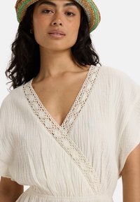 White crinkled fabric dress with a deep V-neck and lace detailing at the neckline. Lightweight, flowy design with short sleeves.